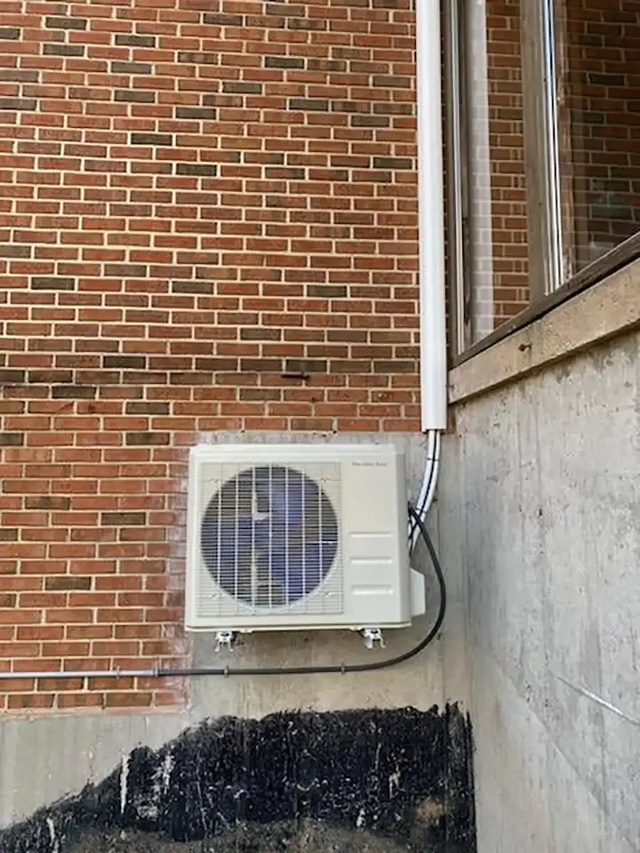 Outdoor AC compressor mounted on brick wall